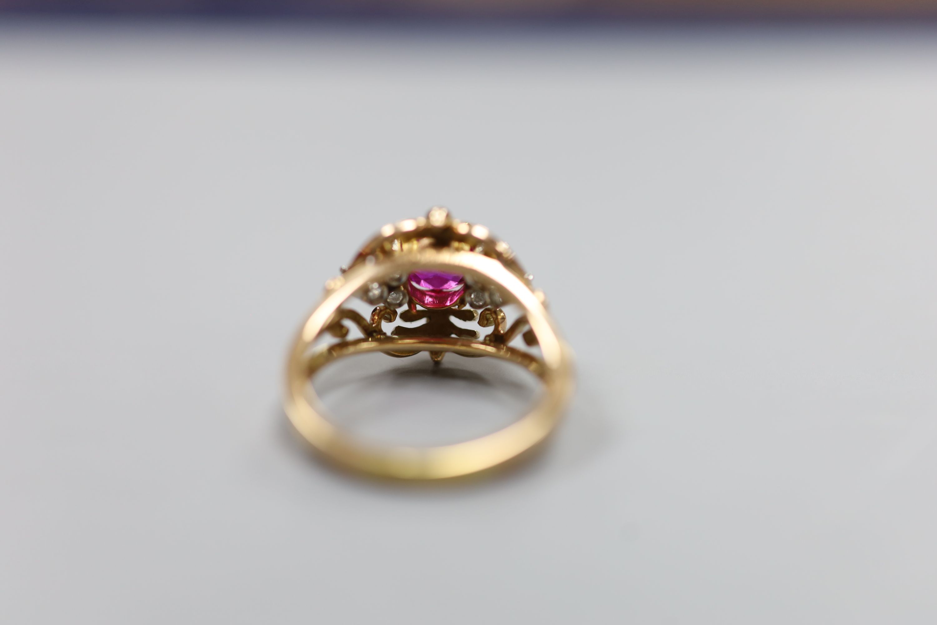 A stylish yellow metal, ruby and diamond set cluster ring, with single round cut ruby(crack), flanked by six round cut diamonds, in an openwork scroll setting, size Q/R, gross weight 7.5 grams, in a Cartier box.